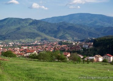 Scenic village nestled in mountains with lush green field and quaint houses.