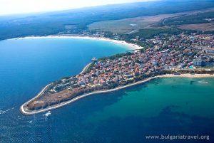 Aerial view of a quaint coastal town with colorful buildings, sandy beaches, and boats in the harbor.