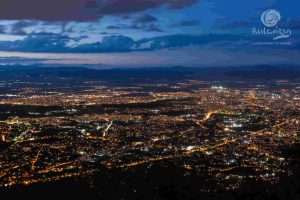 A breathtaking night view of the city, captured from a mountain peak. The city lights twinkle below, creating a mesmerizing sight.