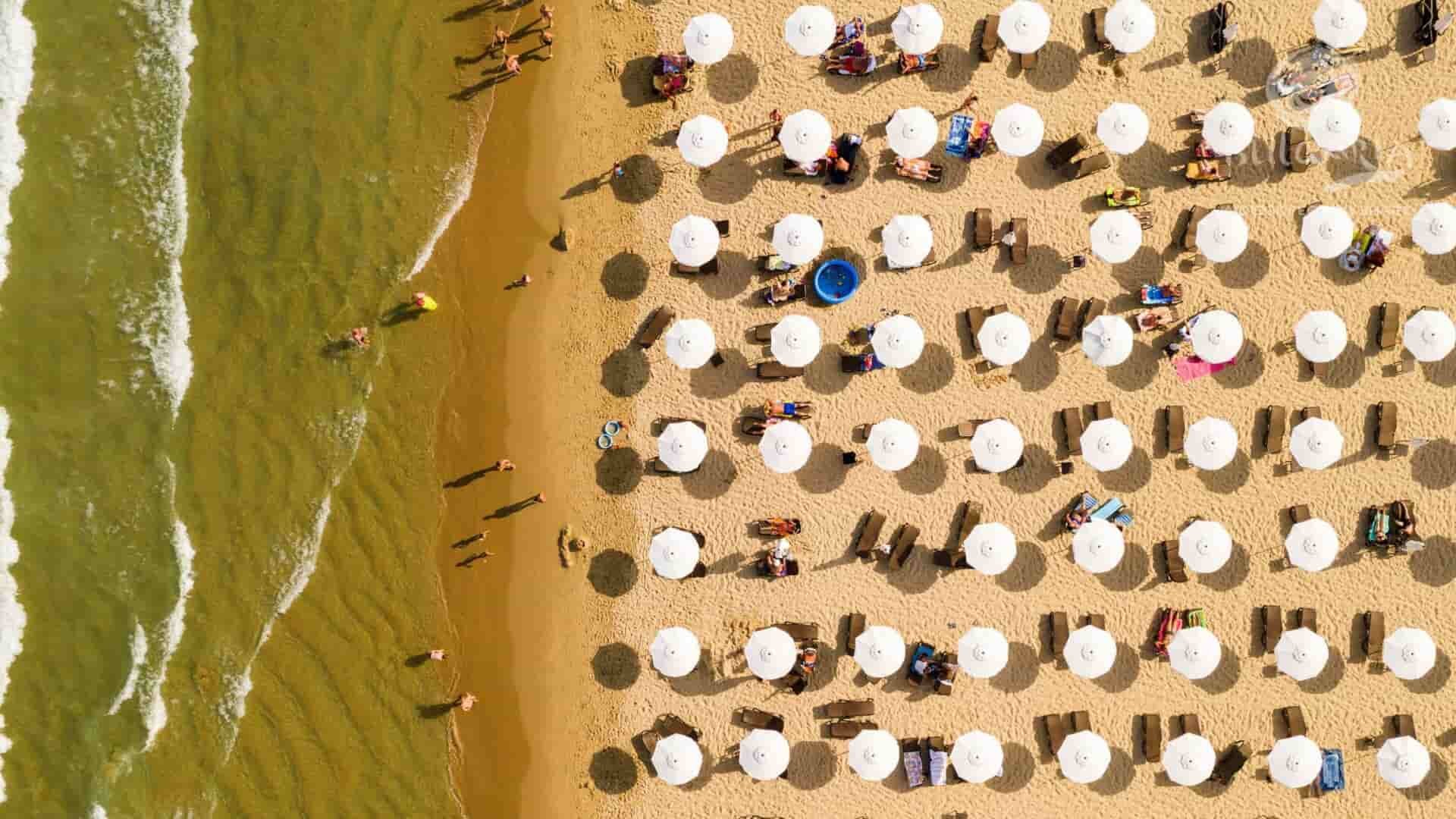 Aerial view of people enjoying a sunny day at the beach, with turquoise waters and golden sand.