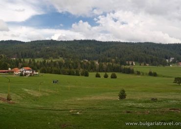 A serene green field with a house in the distance under a clear blue sky.